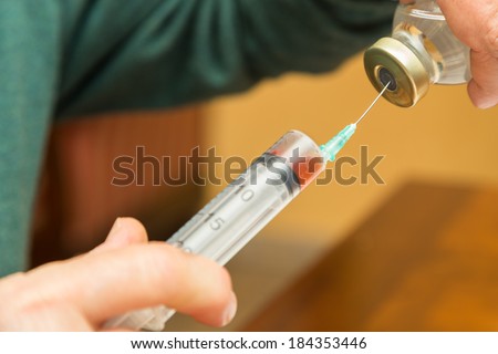 A doctor on call is filling a disposable plastic hypodermic syringe for an injection to his patient