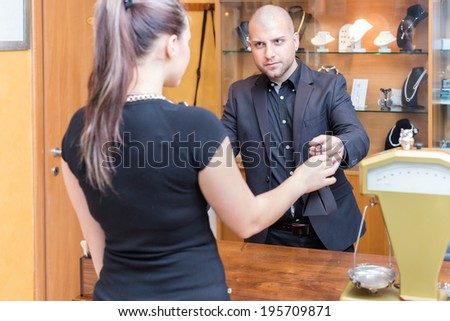Jewelry store owner is passing a sold product to his buyer, a young woman.