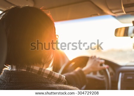 A car woman driver is travelling while the light of the sunset hits her face.