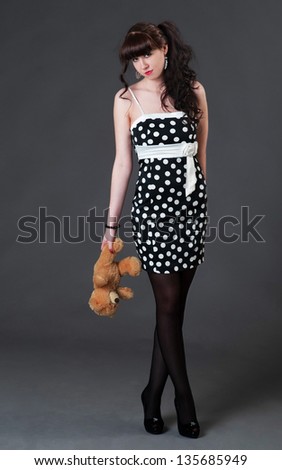 beautiful girl with long dark hair in a narrow dress bowed her head, holding a teddy bear and should cross over legs