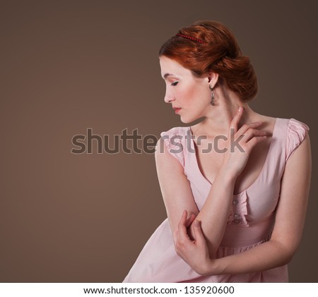 Attractive red hair woman in a pink dress looking down tenderly touches the neck with her hand