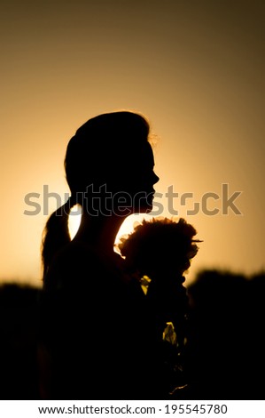 Outline profile of a girl with flowers in hands in rear light at sunset