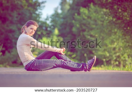 background girl sitting on the asphalt road among green trees arching her back and looking straight summer day