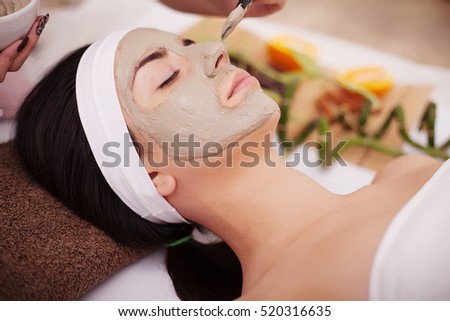 Beautiful young woman receiving gray facial mask in the beauty salon