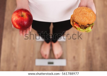 Diet. Woman Measuring Body Weight On Weighing Scale Holding Donut and apple. Sweets Are Unhealthy Junk Food. Dieting, Healthy Eating, Lifestyle. Weight Loss. Obesity. Top View