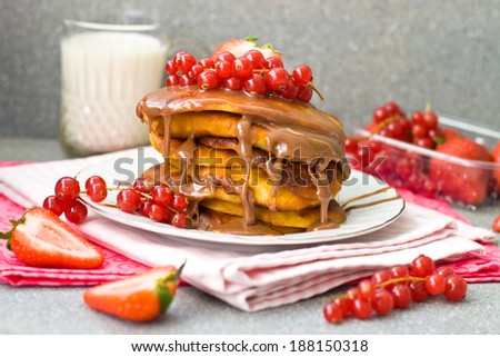 Pancakes with caramel sauce, red currant and strawberries and glass of milk on the grey background, selective focus on the pancakes and caramel