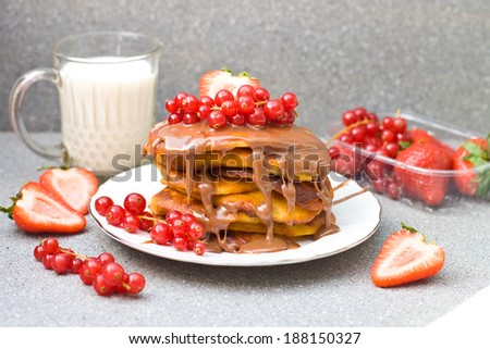 Pancakes with caramel sauce, red currant and strawberries and glass of milk on the grey background, selective focus on the pancakes and caramel