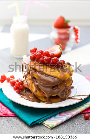 Pancakes with caramel sauce, red currant and strawberries and glass of milk on the grey background