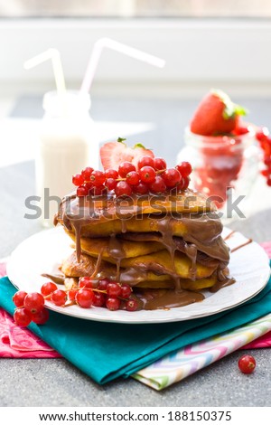Pancakes with caramel sauce, red currant and strawberries and glass of milk on the grey background
