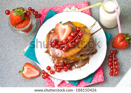 Pancakes with caramel sauce, red currant and strawberries and glass of milk on the grey background, selective focus on the top of the group.