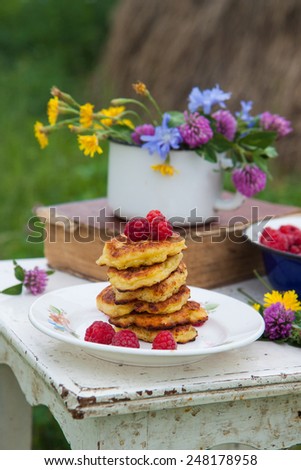 Fluffy cottage cheese pancakes with raspberries, old book and blue bowl with raspberries on the rustic white chair with the haymow on the background.