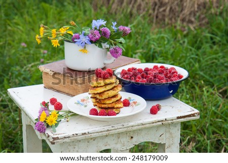 Fluffy cottage cheese pancakes with raspberries, old book and blue bowl with raspberries on the rustic white chair with the haymow on the background.