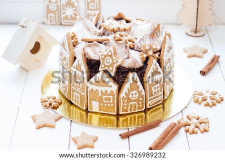Christmas cake decorated with gingerbread house cookies, chocolate swirl meringues and cookie snowflakes on the white background with cinnamon rolls and cookie stars