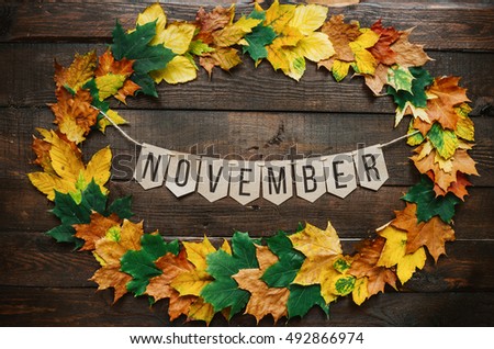 November lettering on paper cardboard eco garland, autumn leafs wreath, dark brown rustic barn wood background.