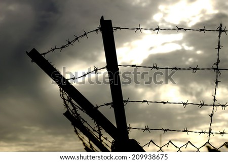 Barbed wire on dark fence. Monochrome silhouette photo