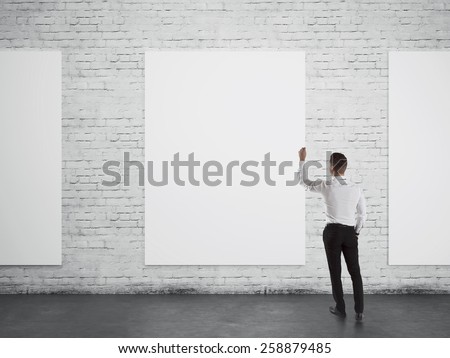 Businessman writing or drawing something on white blank board over brick wall background from back