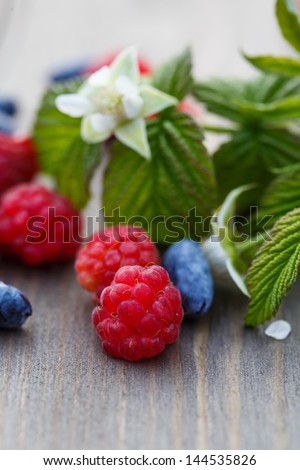 Fresh raspberries and mulberries on a wooden table and a sprig with leaves and raspberry flower