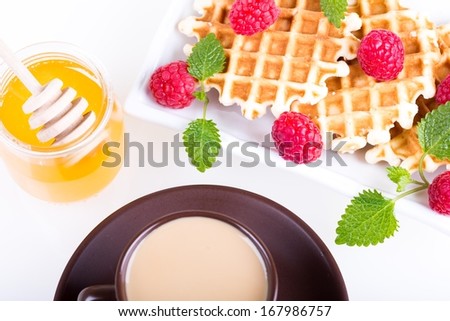 Fresh Belgian waffles with raspberries, honey and cup of coffee on a white background