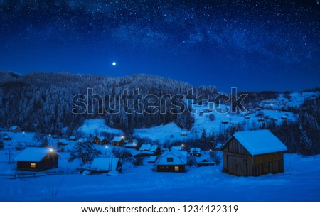 Moonrise in a starry sky over the mountain village covered with fresh snow. Christmas winter night.