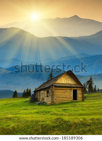 Sunrise in a Carpathian foggy mountain valley with old wooden house on hill