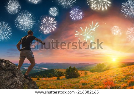 Holiday firework in a sky with hiker, who standing on the top of mountain and points to the sunrise