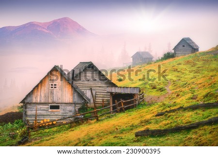 Sunrise above the nature wooden houses in a Carpathian mountains with highest mountain of Ukraine, Goverla. Early misty morning, beginning of new day.