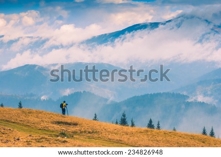 Photographer with backpack stay on a hill and shut mountain landscapes