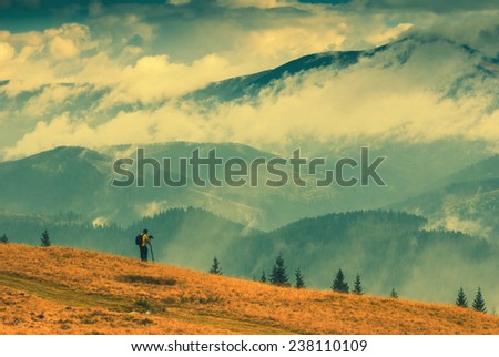 Photographer with backpack stay on a hill and shut mountain landscapes. Vintage colors