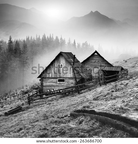 Beautiful sunrise in Carpathian mountains with nature wooden houses on a forest hill. Black and white