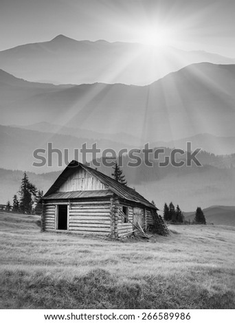 Sunrise in a Carpathian foggy mountain valley with old wooden house on hill. Black and white