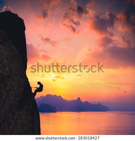 Silhouette of rock climber against sunset over the sea background