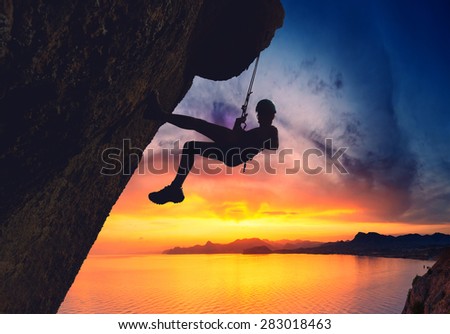 Silhouette of rock climber against sunset over the sea sunset background