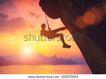 Silhouette of climber on a cliff against beautiful red sunset above the sea