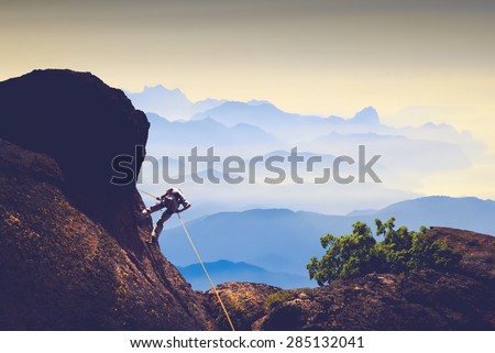 Silhouette of climber on a cliff against misty mountain valley
