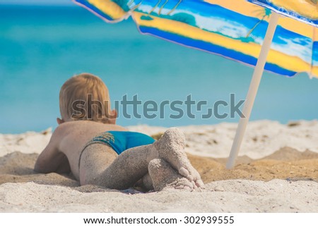 Little kid lying on a sandy beach under umbrella