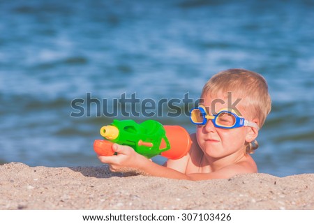 Little boy in a water glasses play with water gun on a sand beach of Black sea