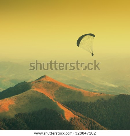 Paraglide silhouette in a light of sunrise above the misty valley. Warm vintage colors