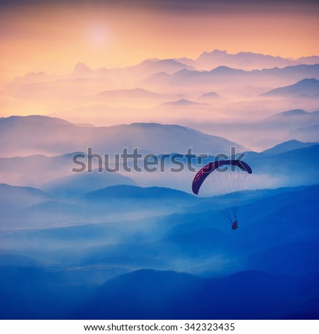 Paraglide silhouette in a light of sunrise above the misty Crimea valley. Vintage colors