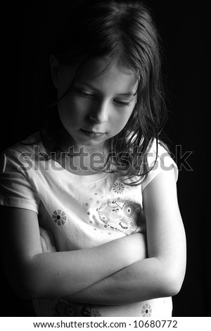 Shot of a pretty seven year old girl looking down with her arms crossed, against a black background