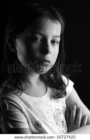 Shot of a pretty seven year old girl looking directly at the camera with her arms crossed, against a black background