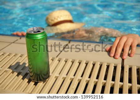 Can of beer by the swimming pool and drowning drunk man in the background