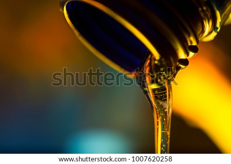 Liquid stream of motor oil flows from the neck of the bottle close-up.