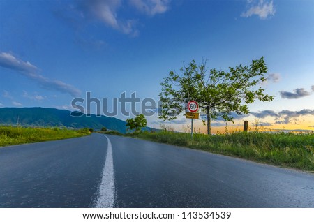 Asphalt road central line between rice fields and trees on the sunset amazing colorful sky, speed limit sign