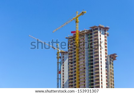 a big yellow crane constructing a new high rise at skyscraper building site at bright clear blue sky