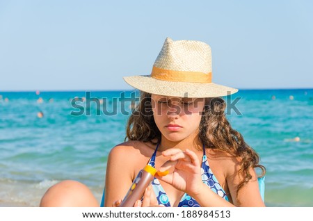 applying sun block cream. beautiful tanned young teen with straw hat and glasses applying sun block cream on hand sitting on a beach