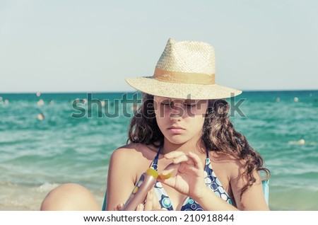 applying sun block cream. beautiful tanned young teen with straw hat and glasses applying sun block cream on hand sitting on a beach, VINTAGE