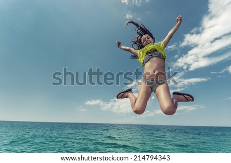 Amazing summer teen jump. Beautiful curly hair girl jumps isolated over ocean water horizon. Clear blue sky and calm water surface.
