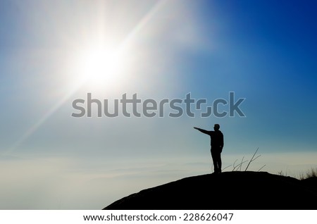 Silhouette of a champion on mountain top pointing toward sun. Sport and active life concept