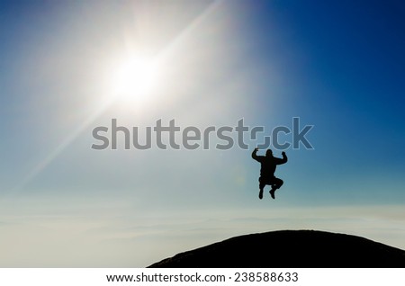 Silhouette of a happy man jumping on mountain top in front of a sunny sky, with room four copy space or text
