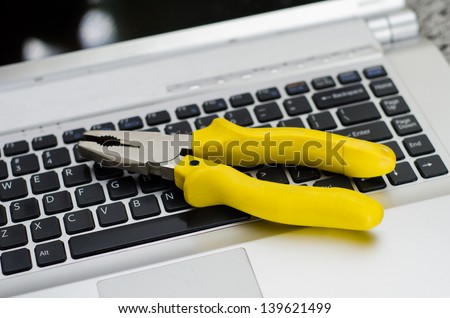 Computer and technology repair suggested by a yellow handled set of pliers on a silver laptop with black keyboard